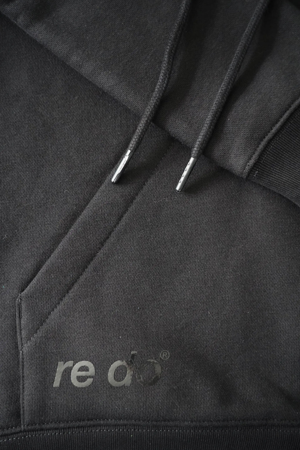Closeup af logo, ærme, ribkant og hættesnore på re do® hoodie sweatshirt i sort