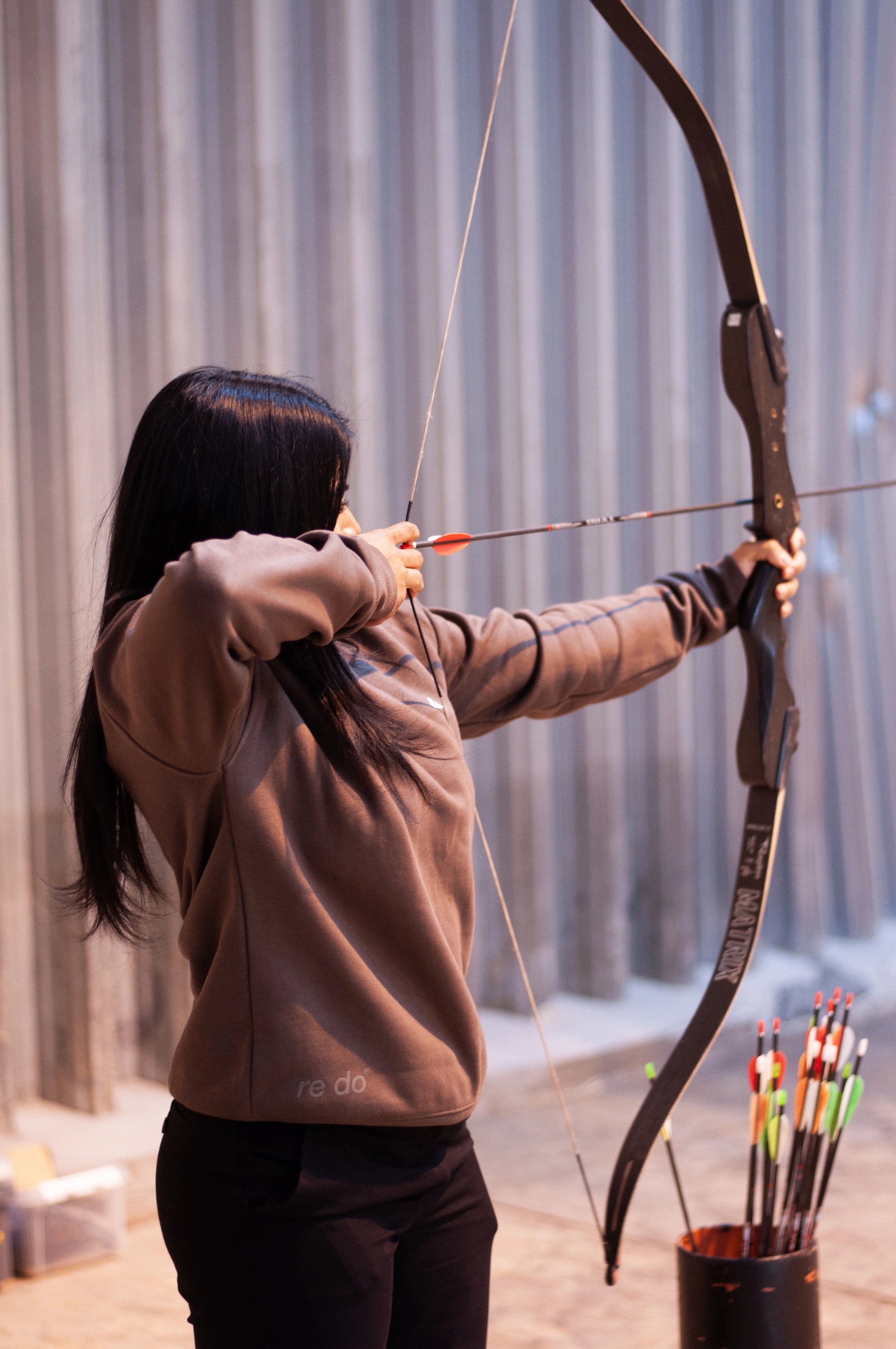 re do x Atlab collab. Person dyrker bueskydning iført firmatøj med tryk fra re do® og sweatshirt med tøj med logo fra re do®.